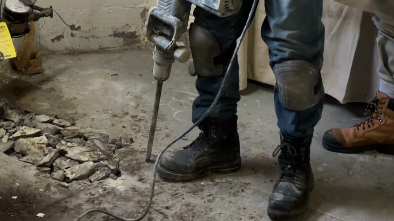 A plumber breaking into a basement slab at night to reach a failed line.